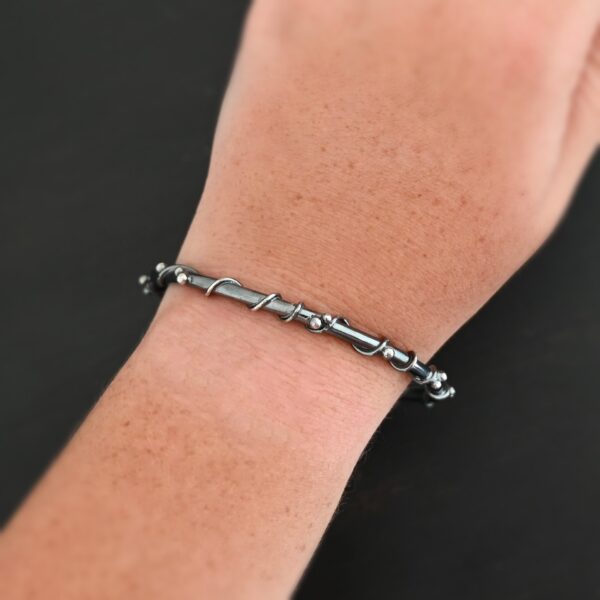 The "Ice Berry" Bangle as shown on a model. Bangle is made out of sterling silver, and has a sterling silver line wrapping around it, as well as silver dots scattered around the bangle. Model is wearing the bangle on wrist to demonstrate the size.