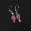 Pink Skies Earrings New Close up of our "Pink Skies" Earrings. Made out of sterling silver and 18k gold, rubies and moissanites. There are two ruby stones and two moissanites. Both ruby stones are oval shaped with points on each end. Both rubies are set in gold. The left earring has a moissanite set in gold on the bottom of it. The right earring has the moissanite on the top of the earring. Both earrings have two small gold dots on them, one on the top of the earring and one on the bottom. Earrings are on gold leverback ear wires.