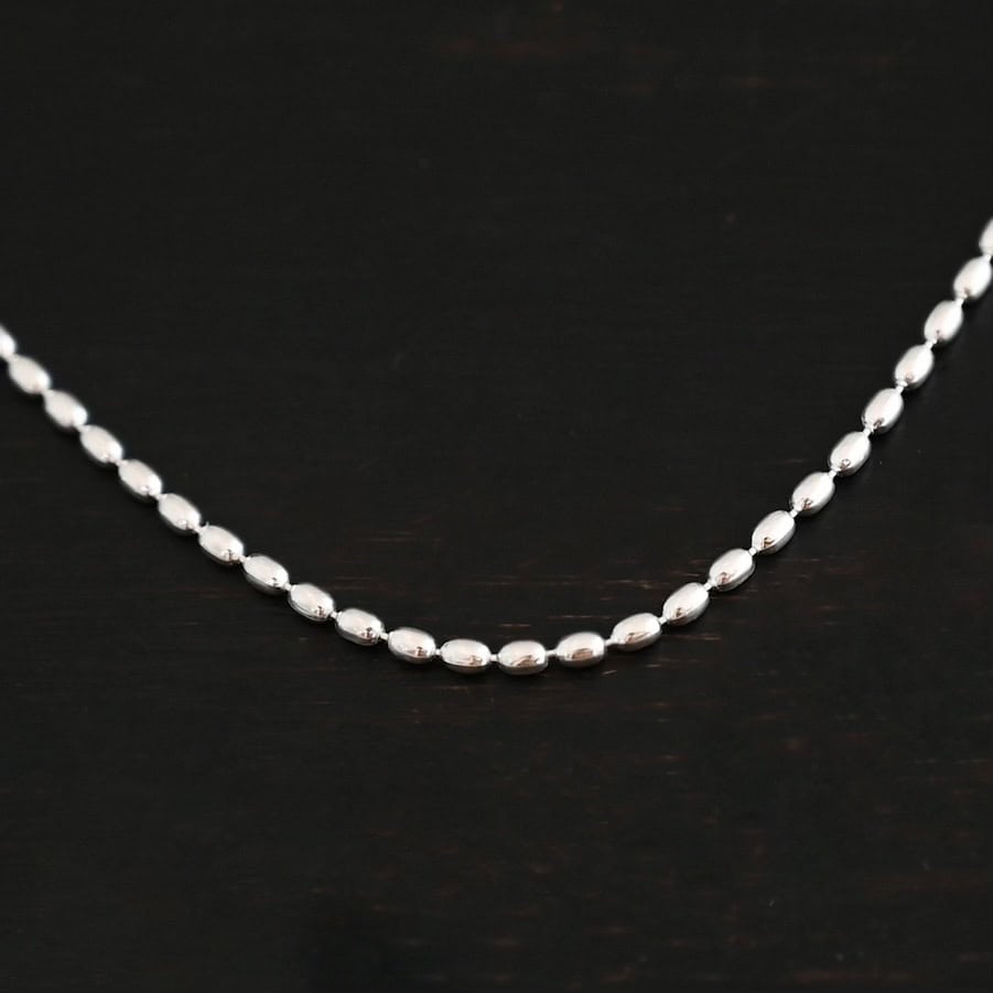 "Bryn Beaded" Chain as shown up close. Chain is shown as shiny with 1.5mm oval beads that have very little space between them. Chain is shown against a dark background.