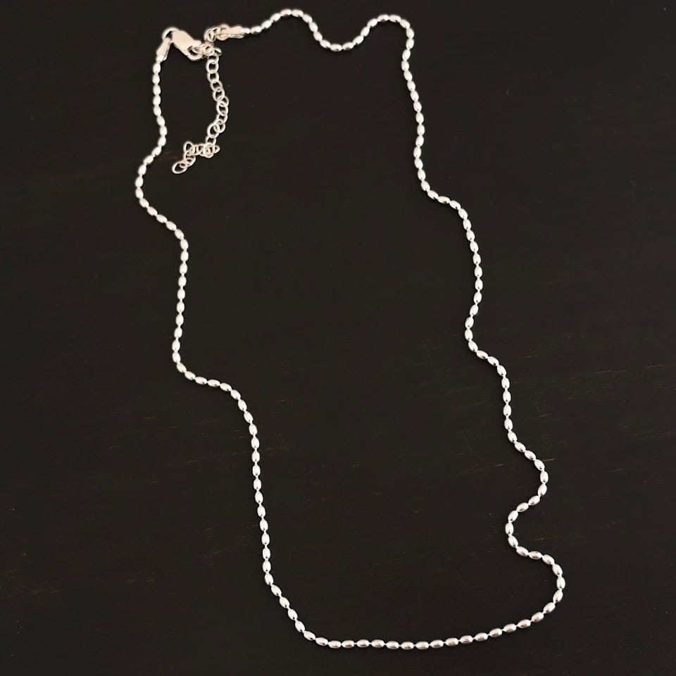 "Bryn Beaded" Chain as shown up close. Chain is shown as shiny with 1.5mm oval beads that have very little space between them. Chain is shown against a dark background. Chain has a lobster claw clasp and a three inch sterling silver extension.