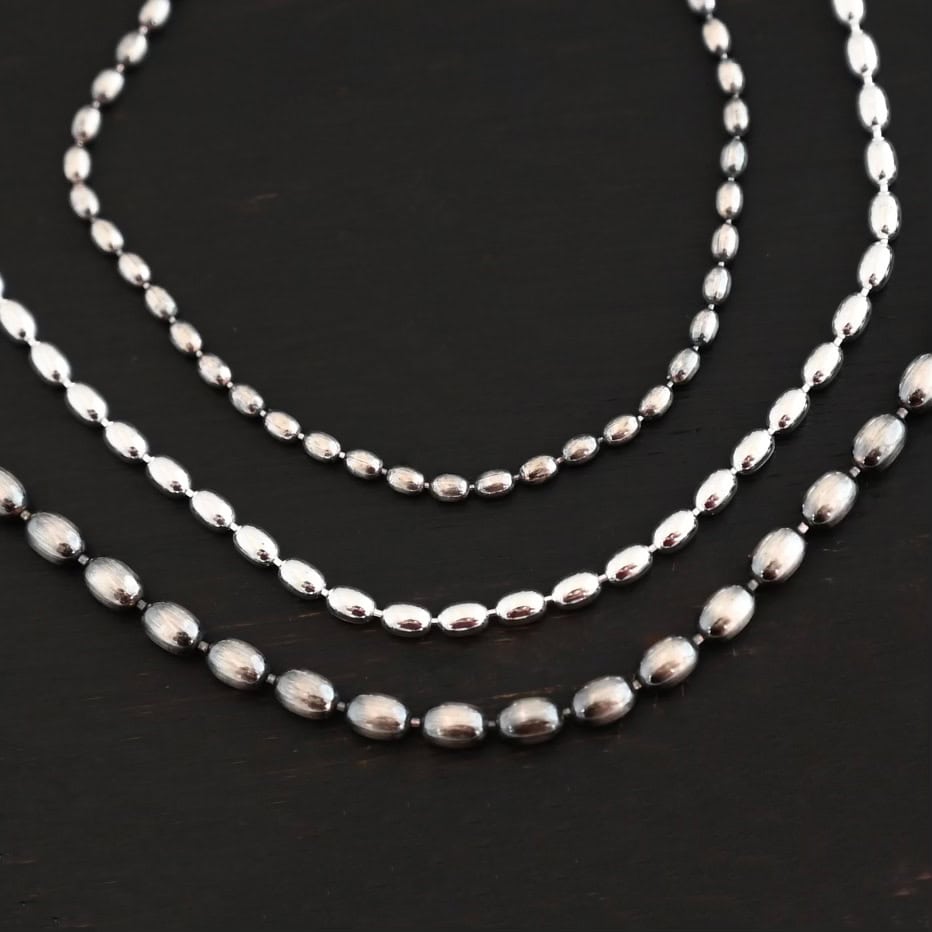 "Bryn Beaded" Chain shown up close in 1.5mm, 2mm, and 3mm. They are set on top of one another to demonstrate how the sizes increase. The top chain is 1.5mm and is oxidized. The next one is 2mm and shiny. The last chain is 3mm and oxidized. All chains are set against a dark background.