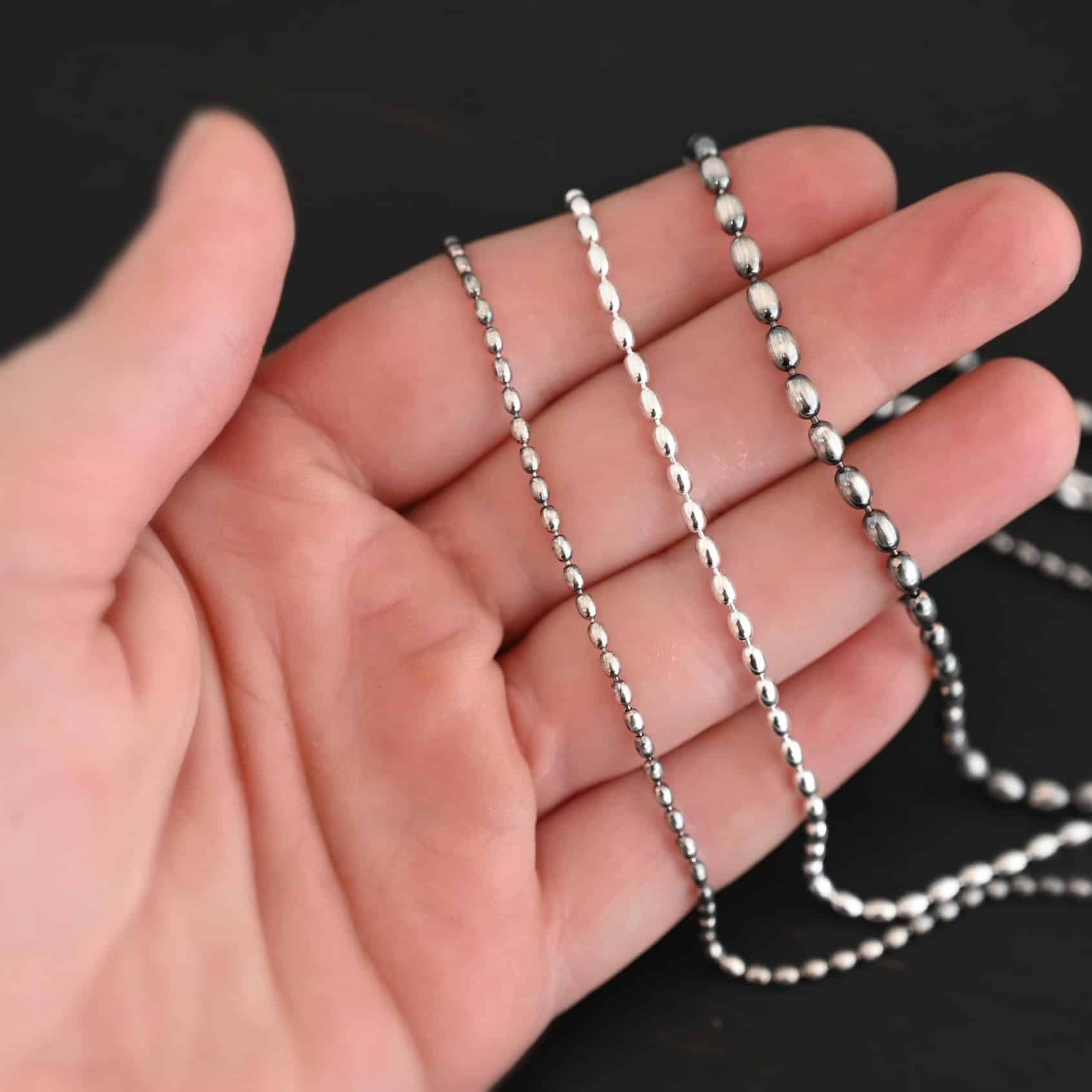 "Bryn Beaded" Chain shown up close in 1.5mm, 2mm, and 3mm. They are set on top of one another to demonstrate how the sizes increase. The top chain is 1.5mm and is oxidized. The next one is 2mm and shiny. The last chain is 3mm and oxidized. Chains are set against the palm of a hand to demonstrate how sizes increase.