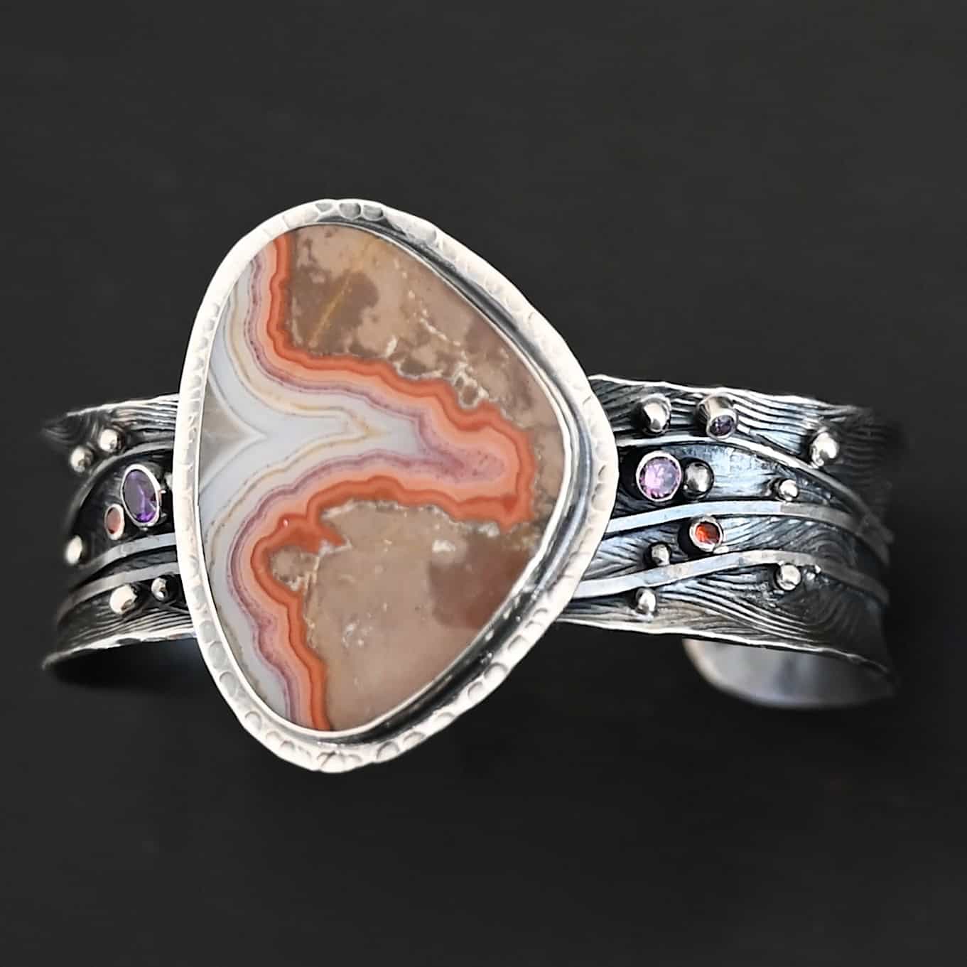 Zion Canyon Cuff "Zion Canyon" Cuff. There is a large, wide, oval, vertical ocean jasper in the center of a very wide, thick cuff. There are wavy lines of silver going across it and multiple gemstones scattered across it, along with silver ball detail. There is hammered silver around the stone.