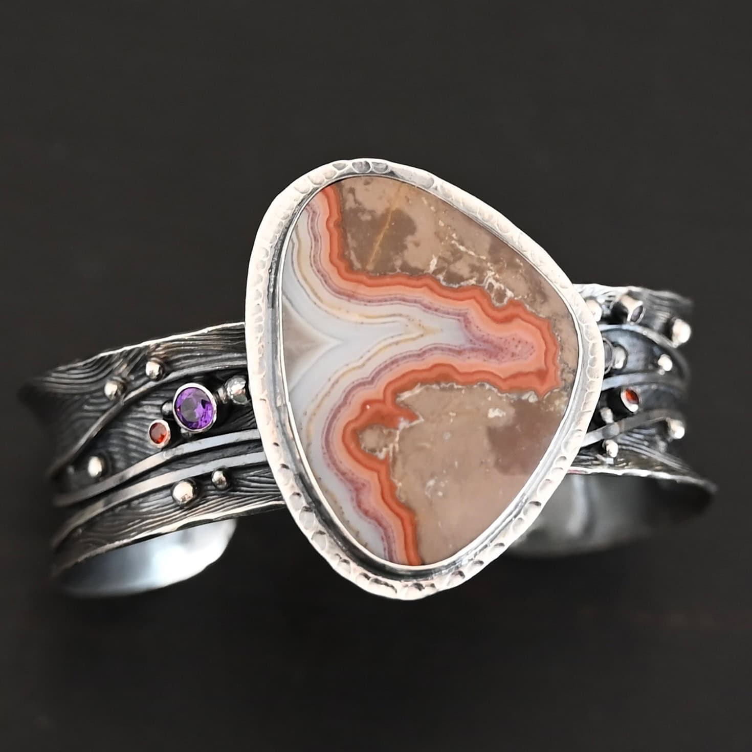 Zion Canyon Cuff "Zion Canyon" Cuff. There is a large, wide, oval, vertical ocean jasper in the center of a very wide, thick cuff. There are wavy lines of silver going across it and multiple gemstones scattered across it, along with silver ball detail. There is hammered silver around the stone.