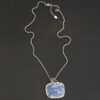 Close up of the "Azula" Necklace. Made out of sterling silver and leland blue. The leland blue is a square shape and is a dark blue color with light gray dots scattered throughout the stone. There is a loop on the back of the pendant that is attached to jump rings that are attached to the chain of the necklace. Pendant is laying against a dark background.
