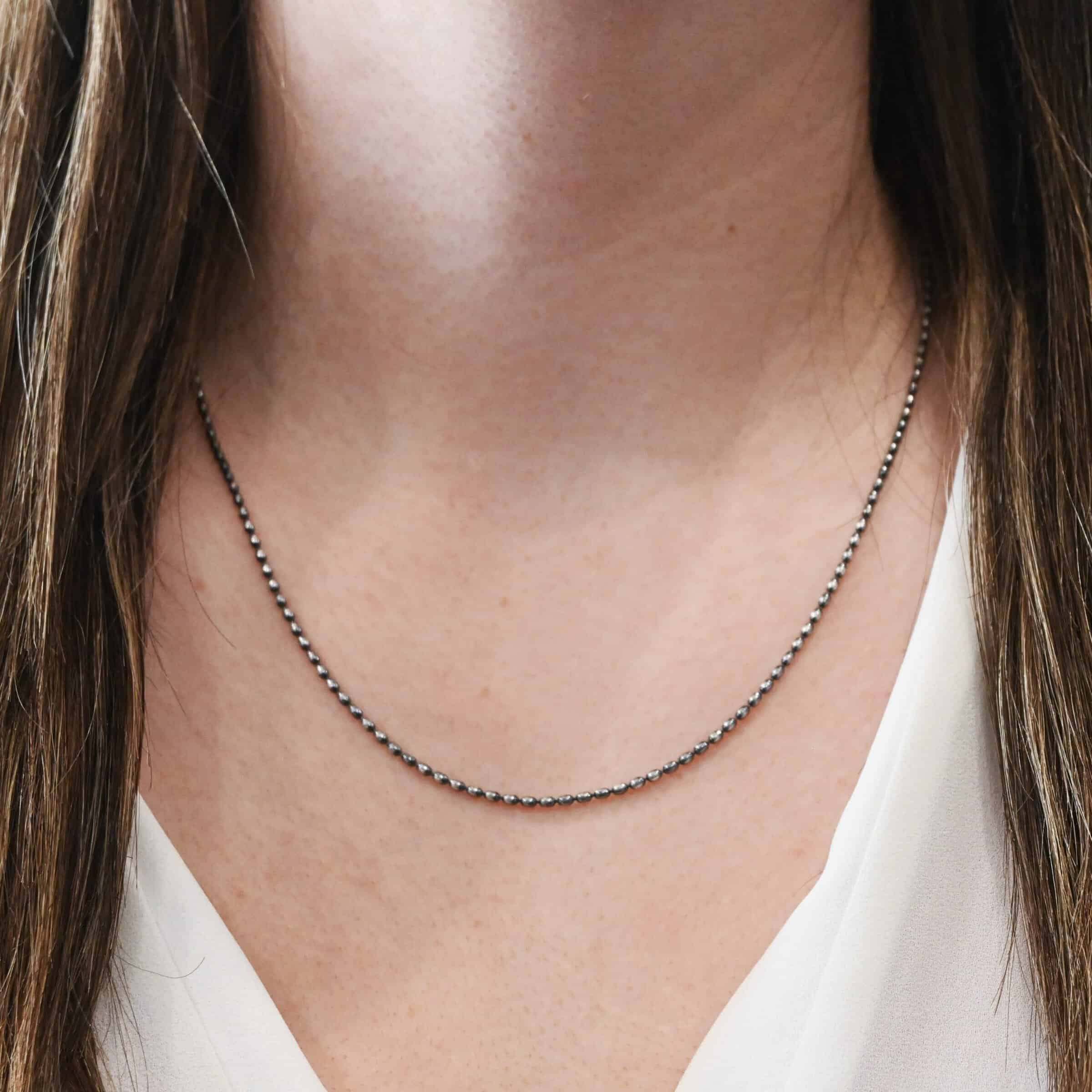 Close up of the "Bryn Beaded" Chain as shown on a model wearing a white v-neck shirt. Chain is shown at 20 inches long and with 1.5mm beads, as well as oxidized.