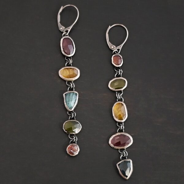 "Living In Color" Earrings as shown up close. Made out of sterling silver and ten sapphires with leverback ear wires. The sapphires are multiple colors. Earrings are set against a dark background.