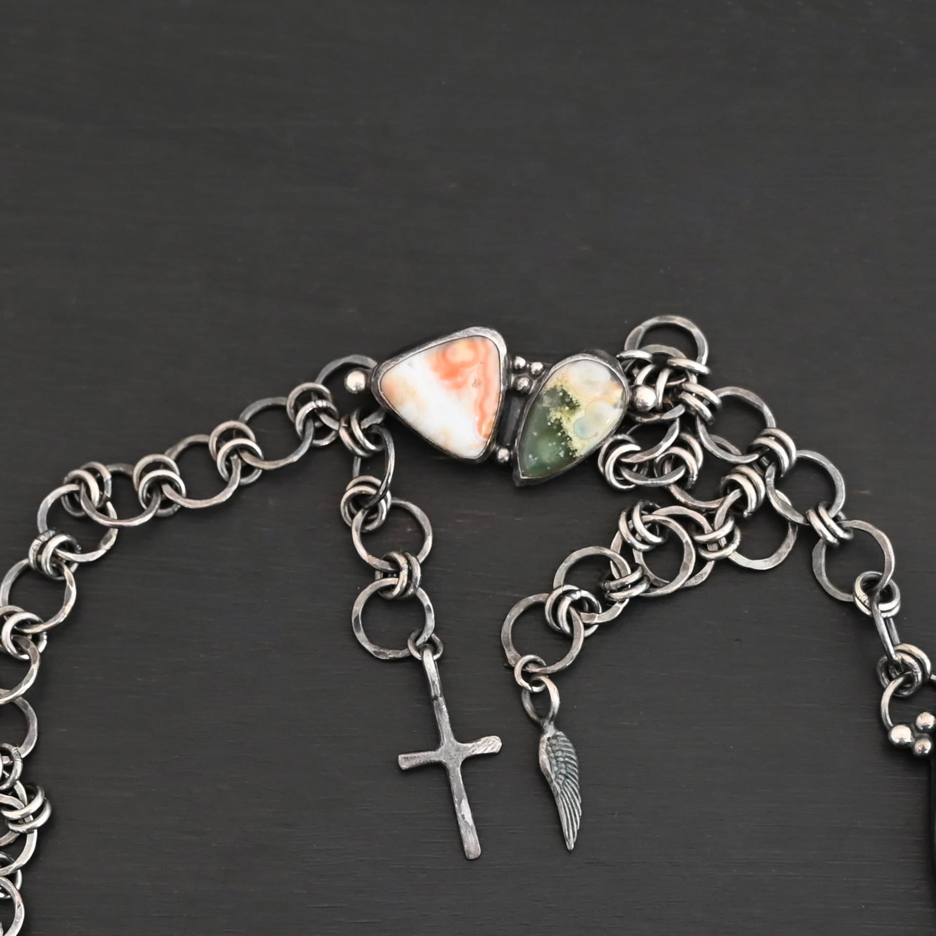 Look For Adventure Necklace New The "Look For Adventure" Necklace clasp. Made out of sterling silver and ocean jasper. There are two ocean jasper that make up the clasp. One is teardrop shaped and the other is triangle shaped. The teardrop shaped ocean jasper is on the left side of the clasp. It is dark green from the tip of the teardrop to the middle of the stone. The bottom half of the stone is yellow with white spots. The triangle shaped ocean jasper is on the right side of the clasp. It is orange from the top point of the triangle to the center. The bottom half of the triangle is white. The clasp is attached to a handmade sterling silver chain that has large circular loops that are hammered and oxidized. The circle loops are attached together with jump rings. Clasp is sitting against a dark background.