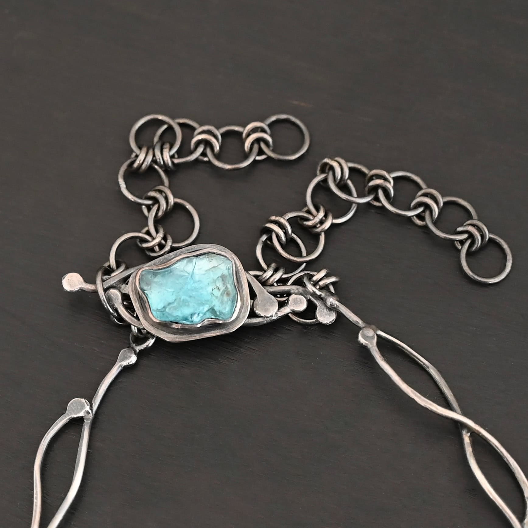 Like The River Runs Necklace New Clasp of the "Like The River Runs" Necklace. Clasp is made out of apatite and is set in sterling silver with silver swirls going around the clasp. Clasp is sitting against a dark background.