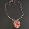 "Inner Planet" Necklace. Made out of Sterling Silver, Teepee Canyon Agate, Garnet & Aquamarine. Agate is the largest stone in a slight oval shape with a slight pointed end. It is a mix of red swirls. The aquamarine is closest to the agate. It is in the top left corner of the necklace. It is small and circular. The garnet is next to the aquamarine. It is oval shaped and a dark red. The stones are soldered to a casted sterling silver branch that is curved to go across the neck.