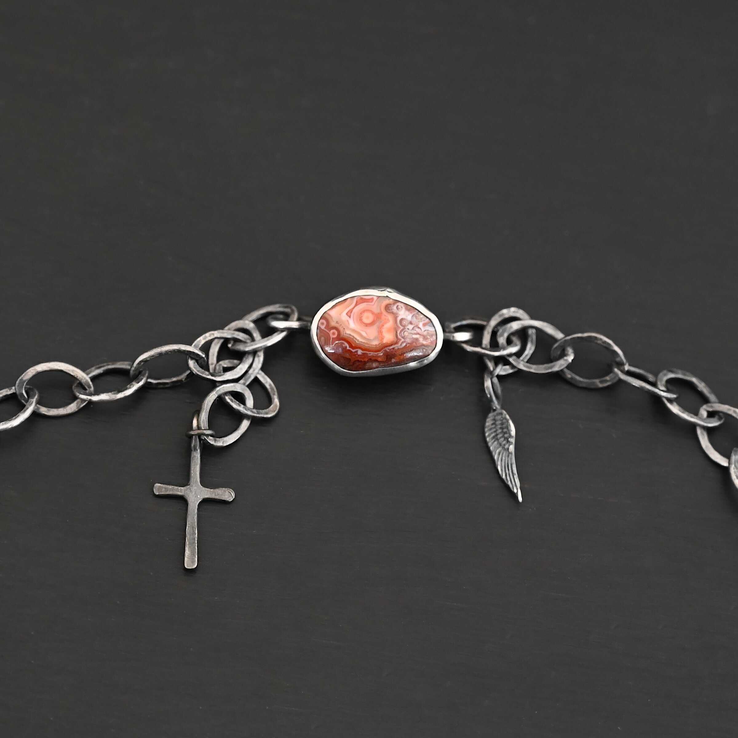 Inner Planet Necklace Clasp for the "Inner Planet" Necklace. There is a small, oval, red, white, and orange agate with two hooks on the back for the links to connect to, as well as a small cross and angel wing charm.