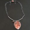 "Inner Planet" Necklace. Made out of Sterling Silver, Teepee Canyon Agate, Garnet & Aquamarine. Agate is the largest stone in a slight oval shape with a slight pointed end. It is a mix of red swirls. The aquamarine is closest to the agate. It is in the top left corner of the necklace. It is small and circular. The garnet is next to the aquamarine. It is oval shaped and a dark red. The stones are soldered to a casted sterling silver branch that is curved to go across the neck.