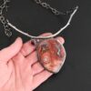 "Inner Planet" Necklace. Made out of Sterling Silver, Teepee Canyon Agate, Garnet & Aquamarine. Agate is the largest stone in a slight oval shape with a slight pointed end. It is a mix of red swirls. The aquamarine is closest to the agate. It is in the top left corner of the necklace. It is small and circular. The garnet is next to the aquamarine. It is oval shaped and a dark red. The stones are soldered to a casted sterling silver branch that is curved to go across the neck.