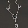 The "Mysteries Beyond" Necklace. Handmade out of sterling silver and five black onyx. Each one is set in sterling silver. There is a black onyx for the clasp of the necklace. There are four bars on each side connected by jump rings that lead to the next two black onyx, one on the left side and one on the right. Then one bar on the right and left lead down to another large black onyx. There is one more bar that leads down to the bottom of the necklace, with one more black onyx. Necklace is set against a black background.