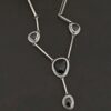 The "Mysteries Beyond" Necklace. Handmade out of sterling silver and five black onyx. Each one is set in sterling silver. There is a black onyx for the clasp of the necklace. There are four bars on each side connected by jump rings that lead to the next two black onyx, one on the left side and one on the right. Then one bar on the right and left lead down to another large black onyx. There is one more bar that leads down to the bottom of the necklace, with one more black onyx. Necklace is set against a black background.