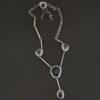 The "Mysteries Beyond" Necklace. Handmade out of sterling silver and five black onyx. Each one is set in sterling silver. There is a black onyx for the clasp of the necklace. There are four bars on each side connected by jump rings that lead to the next two black onyx, one on the left side and one on the right. Then one bar on the right and left lead down to another large black onyx. There is one more bar that leads down to the bottom of the necklace, with one more black onyx. Necklace is set against a black background.