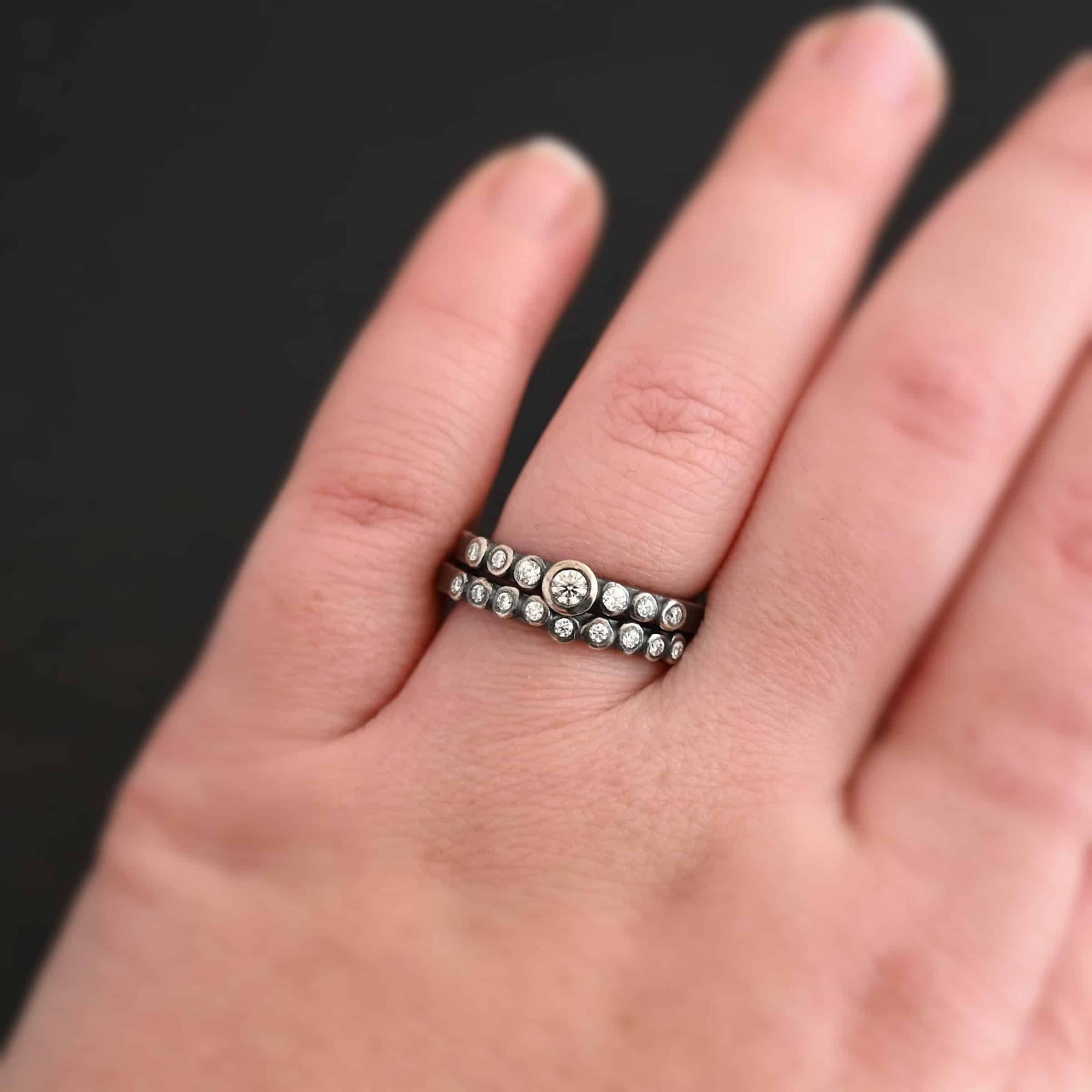New Aura Chic Ring "Aura Chic" Ring as shown up close. Made out of 16 moissanites. There are two bands. The top band contains 7 moissanites. It also contains the largest moissanite, with three on the left side of that and three on the right. The bottom band contains 9 moissanites, all the same size. Ring is worn by a model.