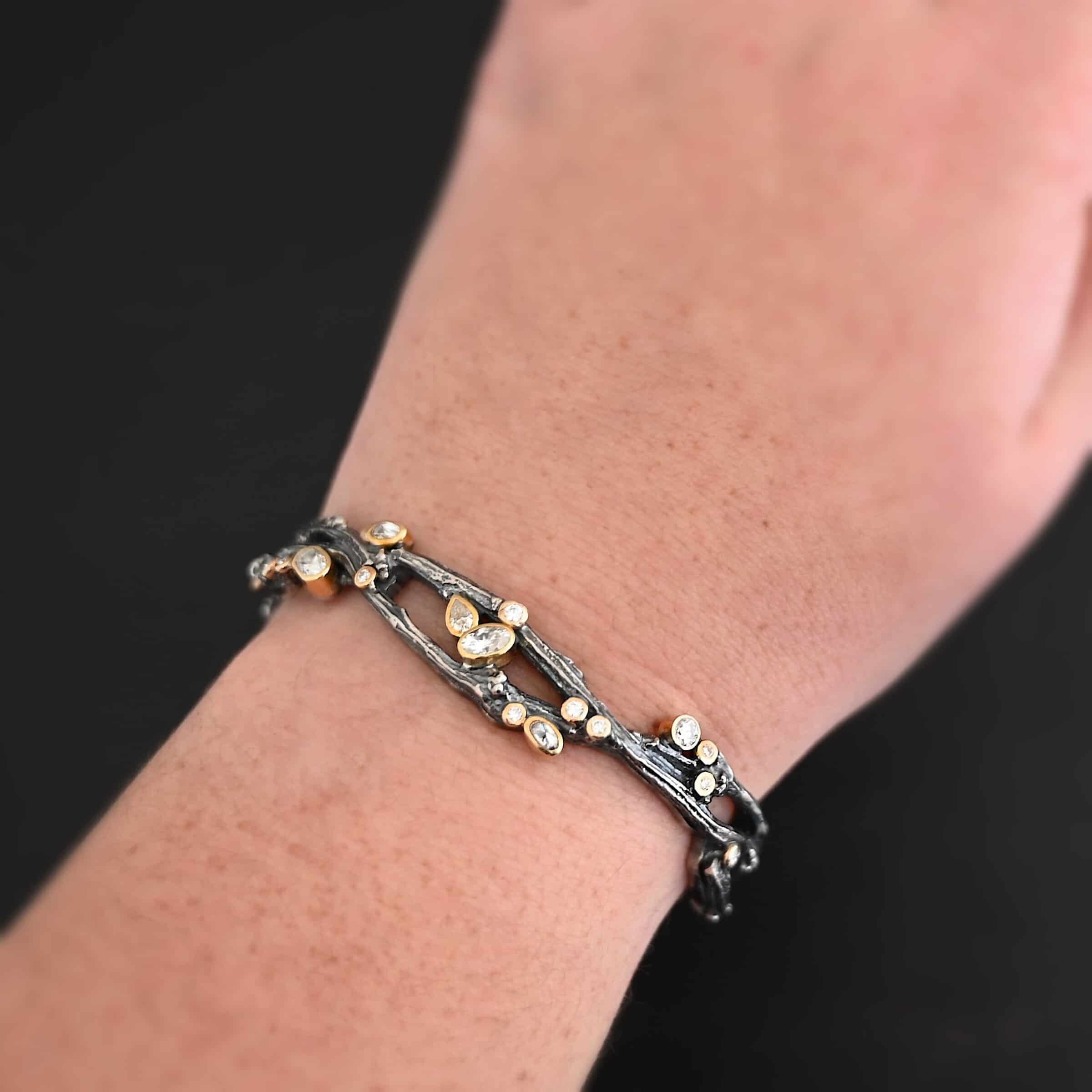 Beautiful Dreams Cuff Close up of the "Beautiful Dreams" Cuff. Made out of sterling silver, gold, and moissanites. There are moissanites set in gold scattered throughout the bracelet. The cuff of the bracelet is made out of sterling silver thick casted twig branches. The branches flow up and down, and intertwine with one another, and the moissanites are set on and in between the branches. Cuff is worn on the wrist of a model to demonstrate thickness of the cuff.