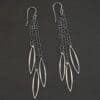 Close up of the "Trickling Rain" Earrings. Made out of sterling silver. Earrings come with french hook ear wires that are sterling silver. Each earring has three strands of chain. On the end of each of these chain strands is a piece of sterling silver that is shaped like an oval, but with pointed ends on each side.
