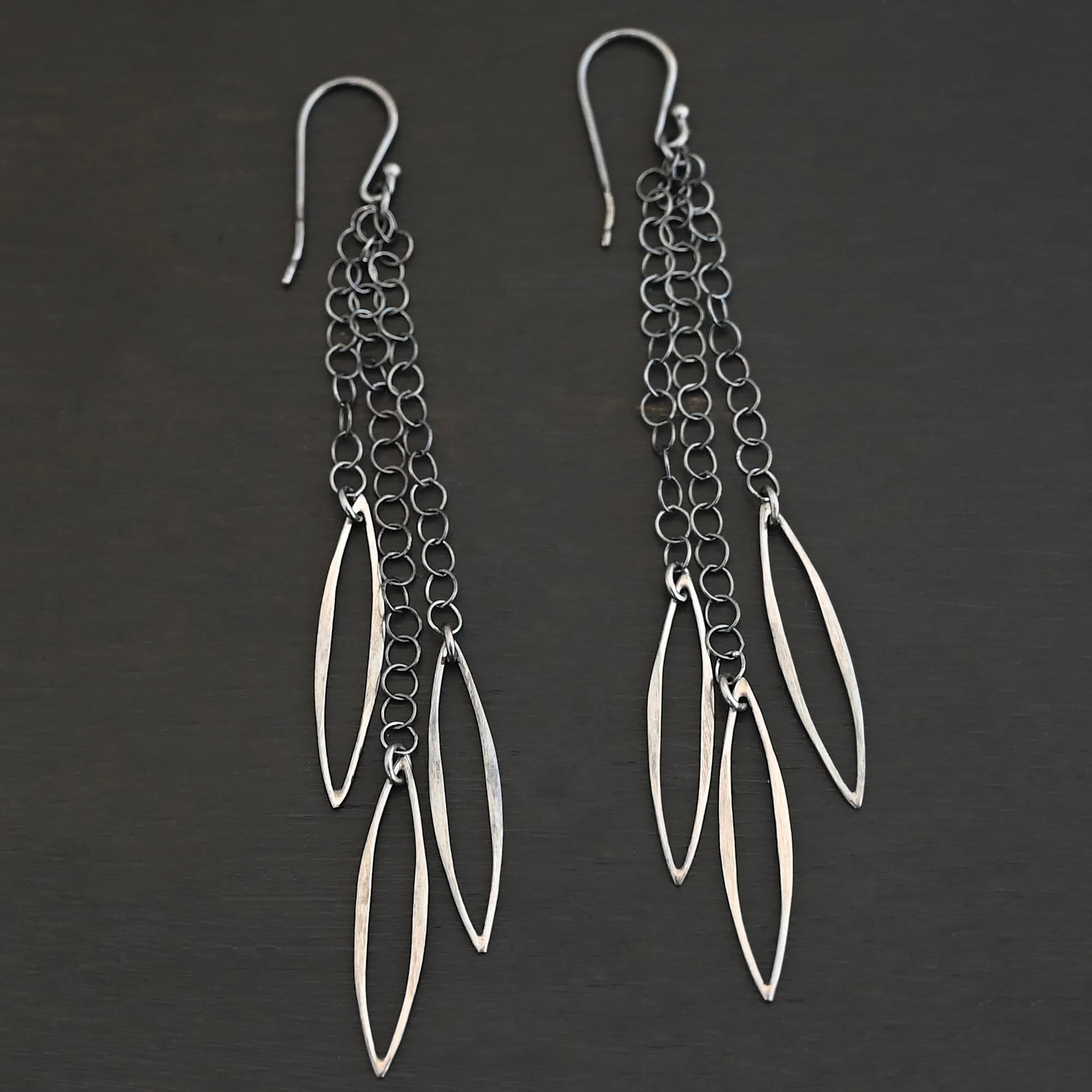 Trickling Rain Earrings New Close up of the "Trickling Rain" Earrings. Made out of sterling silver. Earrings come with french hook ear wires that are sterling silver. Each earring has three strands of chain. On the end of each of these chain strands is a piece of sterling silver that is shaped like an oval, but with pointed ends on each side.