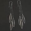 Close up of the "Trickling Rain" Earrings. Made out of sterling silver. Earrings come with french hook ear wires that are sterling silver. Each earring has three strands of chain. On the end of each of these chain strands is a piece of sterling silver that is shaped like an oval, but with pointed ends on each side.