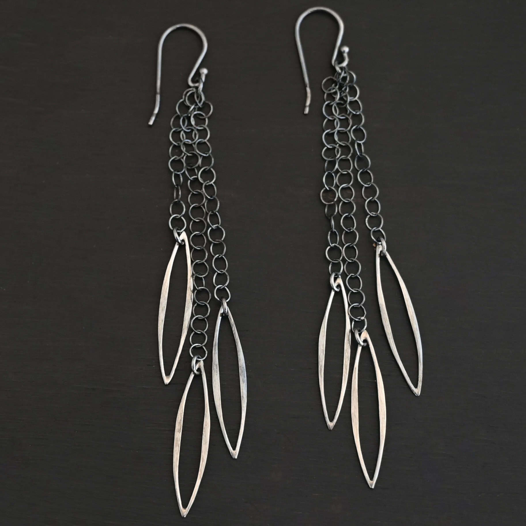 Trickling Rain Earrings New Close up of the "Trickling Rain" Earrings. Made out of sterling silver. Earrings come with french hook ear wires that are sterling silver. Each earring has three strands of chain. On the end of each of these chain strands is a piece of sterling silver that is shaped like an oval, but with pointed ends on each side.