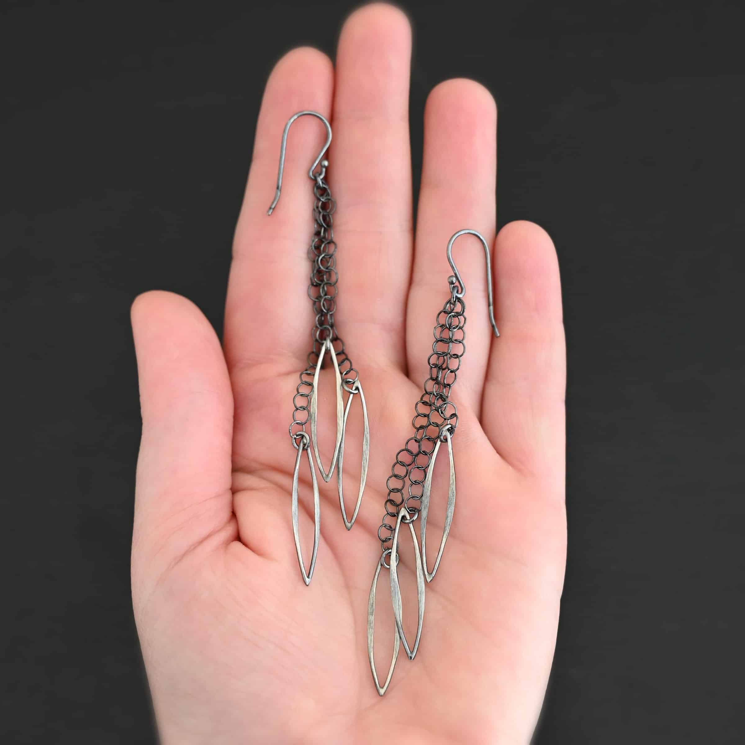 Trickling Rain Earrings New Close up of the "Trickling Rain" Earrings. Made out of sterling silver. Earrings come with french hook ear wires that are sterling silver. Each earring has three strands of chain. On the end of each of these chain strands is a piece of sterling silver that is shaped like an oval, but with pointed ends on each side.