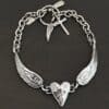 Close up of the "Courage" Bracelet. Bracelet is made out of solid sterling silver with a casted heart and two angel wings. Casted heart is solid sterling silver, and connected by an angel wing on each side. Angel wings are connected to a chain with a toggle clasp to connect the bracelet together. Bracelet is oxidized and the heart is hammered to give it a textured look. Bracelet is set against a dark background.