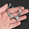 Close up of the "Courage" Bracelet. Bracelet is made out of solid sterling silver with a casted heart and two angel wings. Casted heart is solid sterling silver, and connected by an angel wing on each side. Angel wings are connected to a chain with a toggle clasp to connect the bracelet together. Bracelet is oxidized and the heart is hammered to give it a textured look. Bracelet is set against a dark background.