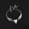 "Courage" Bracelet as shown in shiny. Bracelet is made out of solid sterling silver with a casted heart and two angel wings. Casted heart is solid sterling silver, and connected by an angel wing on each side. Angel wings are connected to a chain with a toggle clasp to connect the bracelet together. The heart is hammered to give it a textured look. Bracelet is shown against a dark background.
