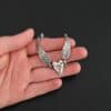 "Courage" Bracelet as shown in shiny. Bracelet is made out of solid sterling silver with a casted heart and two angel wings. Casted heart is solid sterling silver, and connected by an angel wing on each side. Angel wings are connected to a chain with a toggle clasp to connect the bracelet together. The heart is hammered to give it a textured look. Bracelet is shown against a models fingertips to demonstrate size.