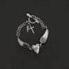 "Courage" Bracelet as shown in oxidized. Bracelet is made out of solid sterling silver with a casted heart and two angel wings. Casted heart is solid sterling silver, and connected by an angel wing on each side. Angel wings are connected to a chain with a toggle clasp to connect the bracelet together. The heart is hammered to give it a textured look. Bracelet is set against a dark background.