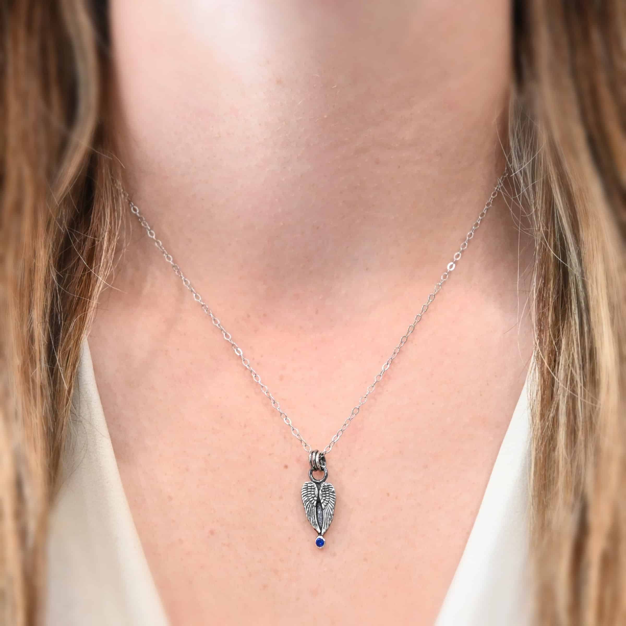 The "Strength" Birthstone Necklace as shown on model. Shown as sterling silver, oxidized, and with a sapphire for the birthstone. Necklaces comes on a "Cassandra" Chain with 2x2mm links. Model is wearing a white v-neck shirt.