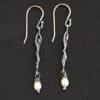 Close up of the "Goddess" Earrings. These earrings are made out of sterling silver and pearls with french hook ear wires. The earrings are sterling silver "women". The pearl hangs from the bottom of the earrings. The pearl is wrapped with sterling silver that is shiny. The rest of the sterling silver is oxidized. Earrings are shown against a dark background.