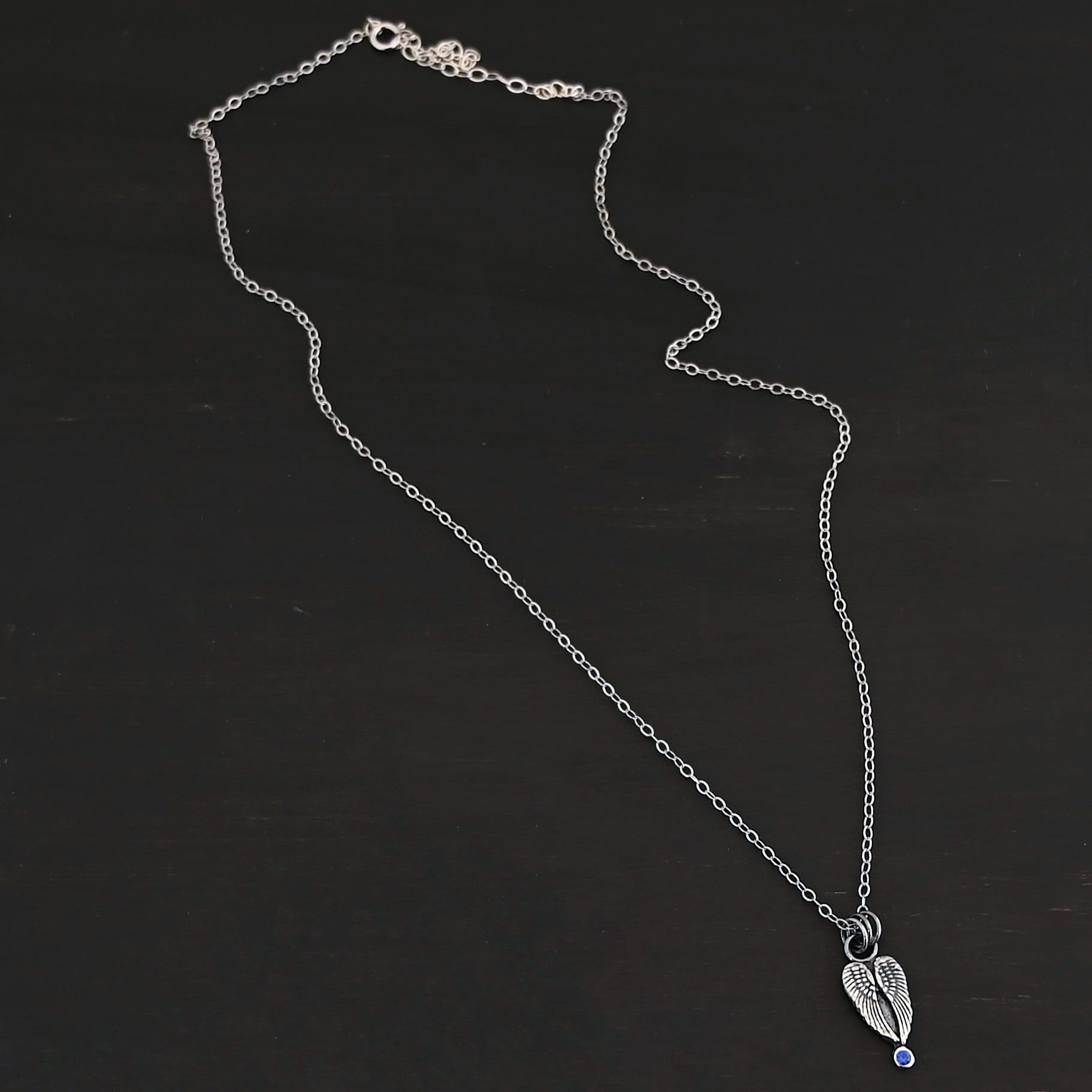The "Strength" Birthstone Necklace. Shown as sterling silver, oxidized, and with a sapphire for the birthstone. Necklace comes on a "Cassandra" Chain with 2x2mm links. Necklace is set against a dark background.