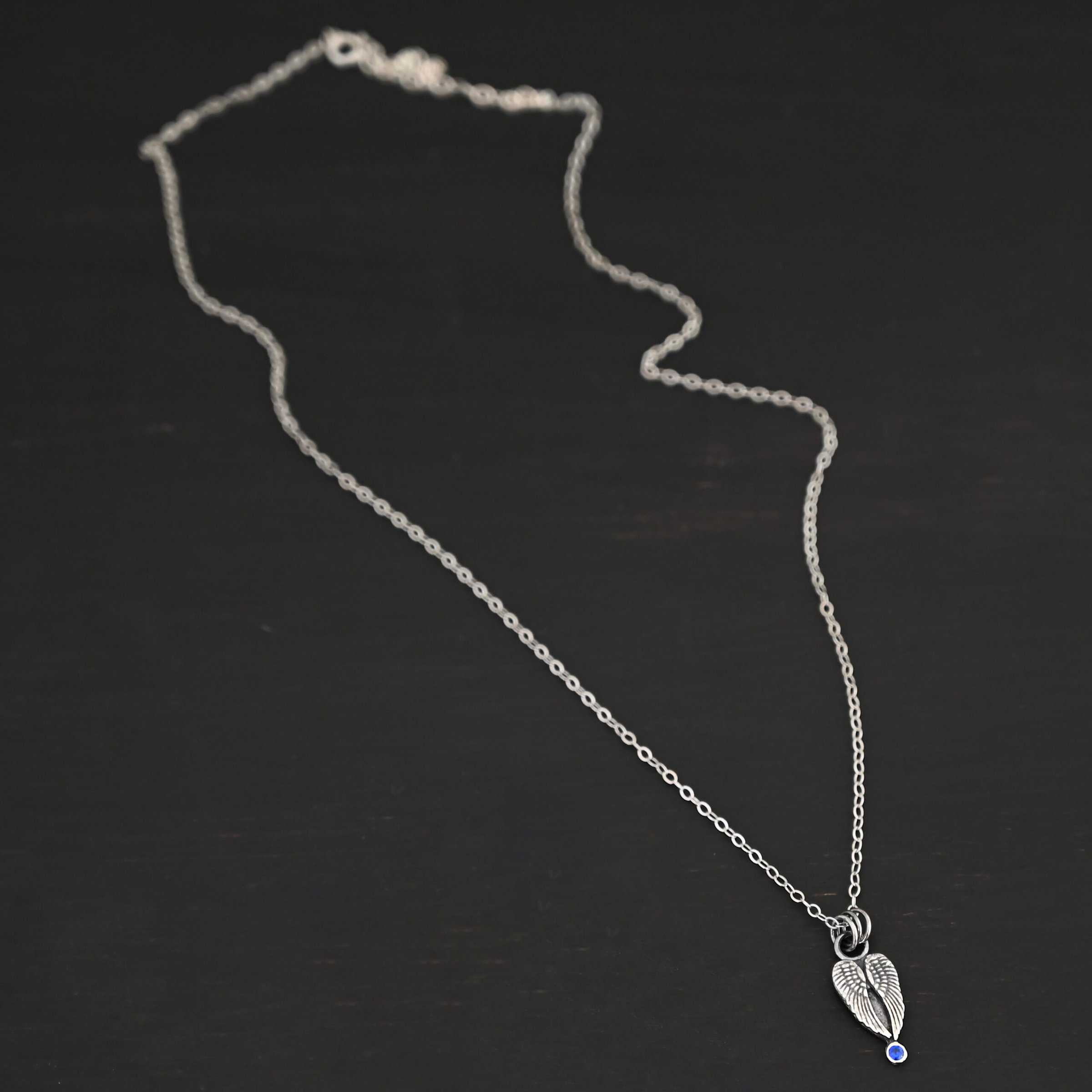 The "Strength" Birthstone Necklace. Shown as sterling silver, oxidized, and with a sapphire for the birthstone. Necklace comes on a "Cassandra" Chain with 2x2mm links. Necklace is set against a dark background.