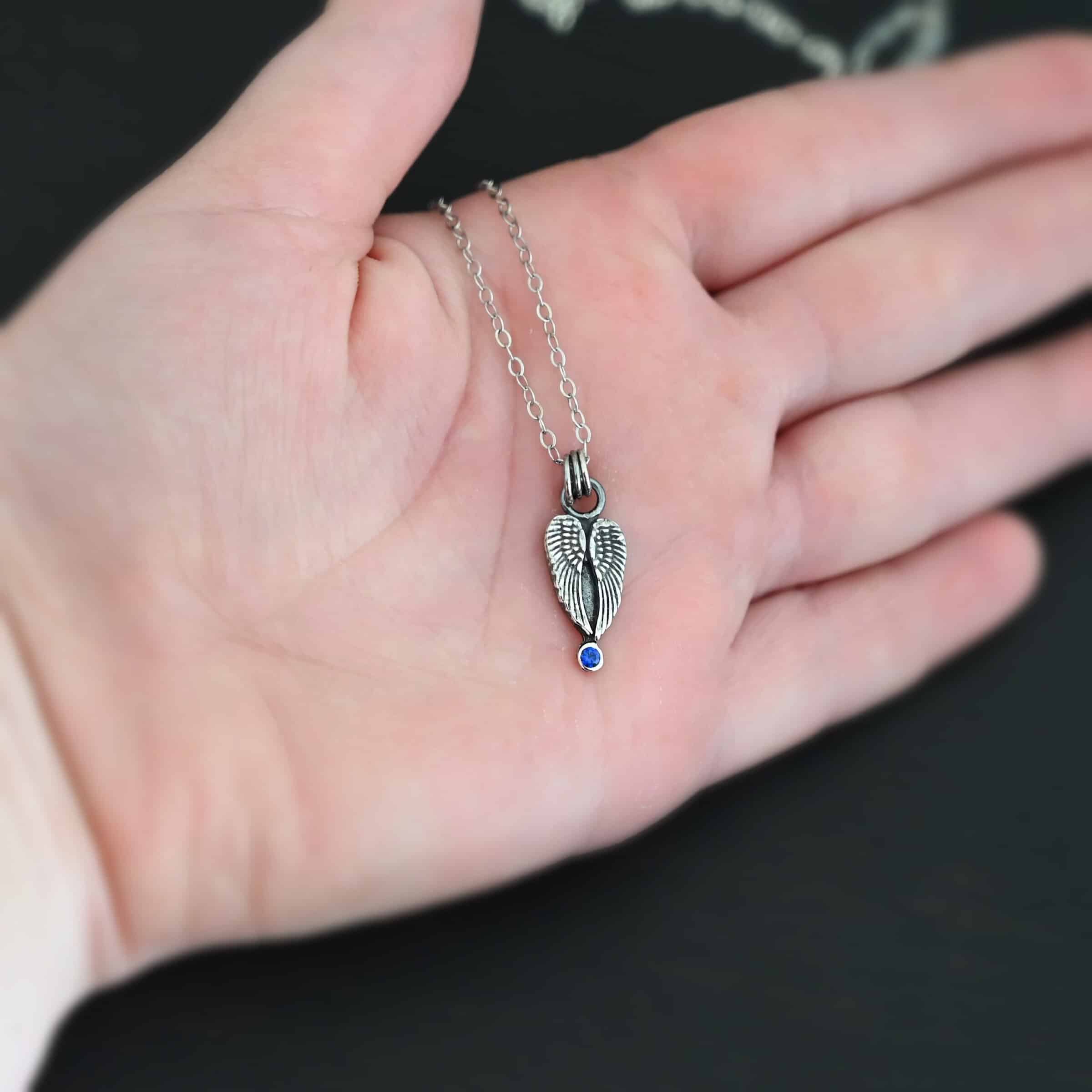 The "Strength" Birthstone Necklace. Shown as sterling silver, oxidized, and with a sapphire for the birthstone. Necklace comes on a "Cassandra" Chain with 2x2mm links. Necklace is set on the palm of a hand to demonstrate the size. Hand is resting against a dark background.