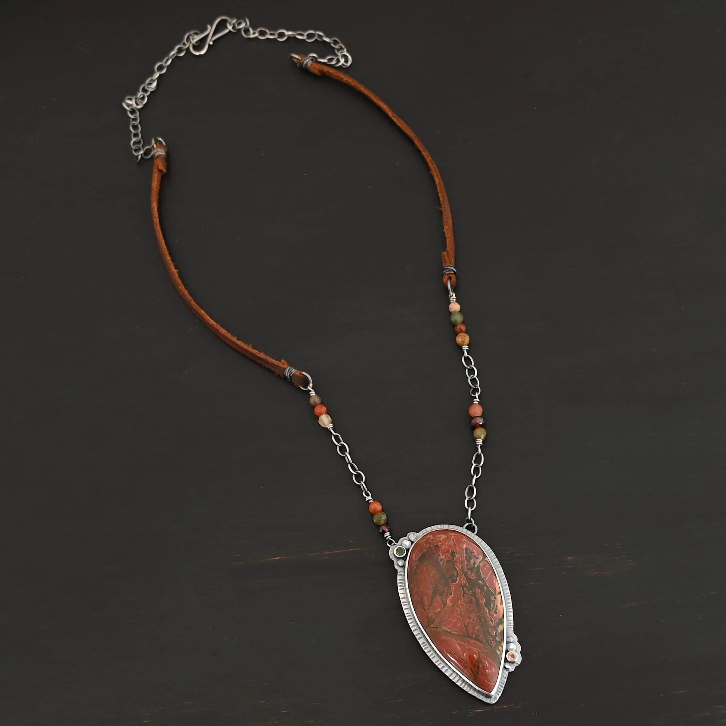 Sunset Orchard Necklace "Sunset Orchard" Necklace. This necklace is made out of sterling silver, cherry creek jasper, and tourmaline. The cherry creek jasper is a large teardrop shape in a sterling silver setting, and there are two tourmalines, one on top of the pendant, and one closer to the bottom. The pendant is attached to a sterling silver chain with beads on both sides.