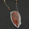 "Sunset Orchard" Necklace. This necklace is made out of sterling silver, cherry creek jasper, and tourmaline. The cherry creek jasper is a large teardrop shape in a sterling silver setting, and there are two tourmalines, one on top of the pendant, and one closer to the bottom. The pendant is attached to a sterling silver chain with beads on both sides.