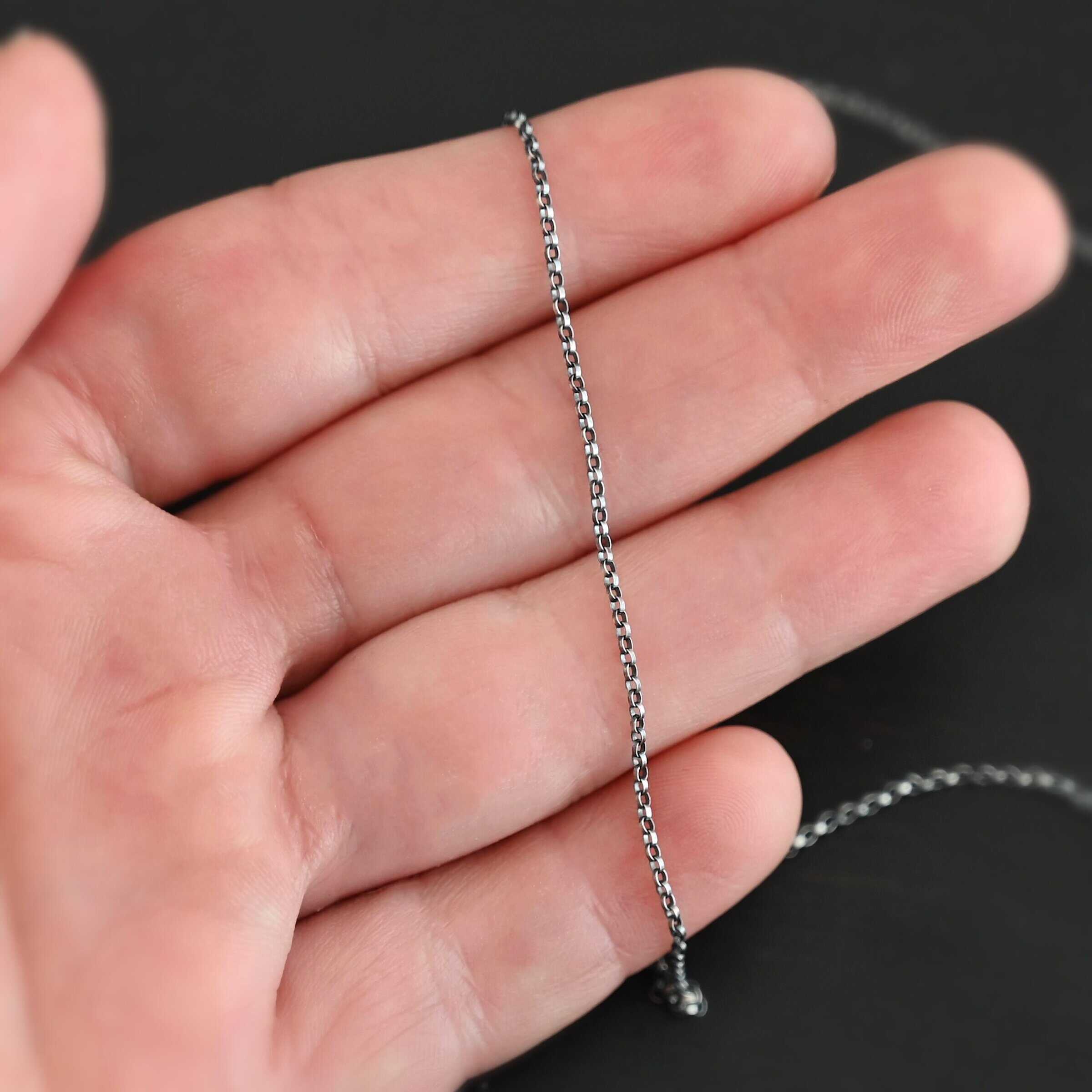 Cassie Chain "Cassie" Chain. The chain is very small oval links that connect together. Chain is oxidized. Chain is shown in the fingertips of a hand.