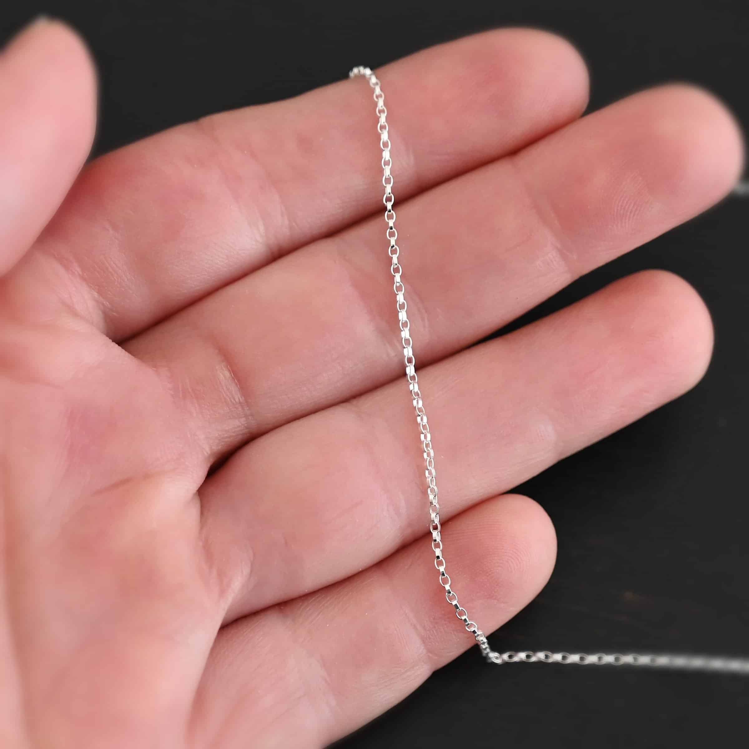 Cassie Chain "Cassie" Chain. The chain is very small oval links that connect together. Chain is shiny. Chain is shown in the fingertips of a hand.