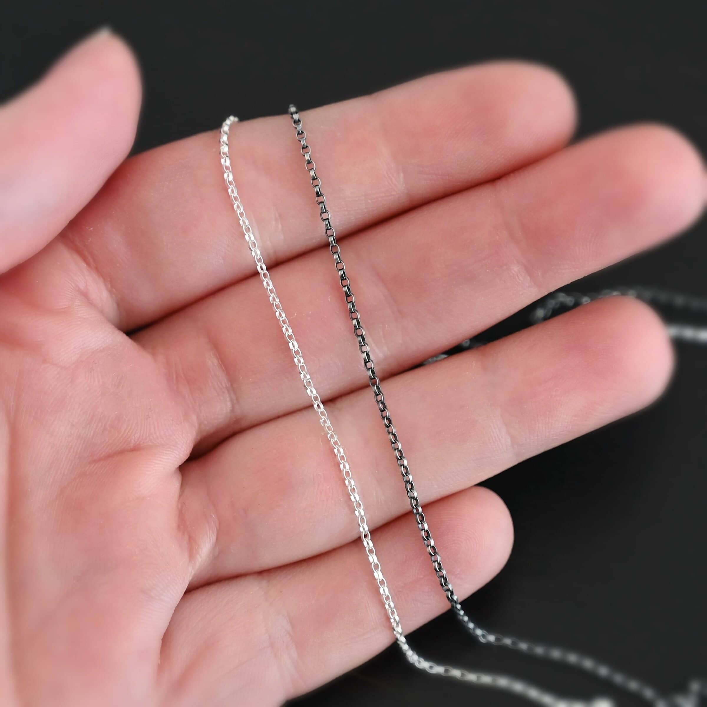 Cassie Chain "Cassie" Chain. The chain is very small oval links that connect together. Chain is oxidized and shiny. Chain is shown in the fingertips of a hand.