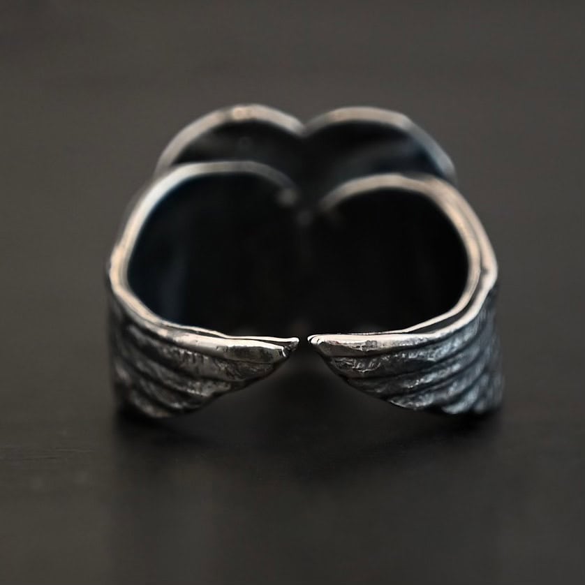 Untamable Spirit Ring Close up of the back of the "Untamable Spirit" Ring. A curved angel wing creates each side of the band and they meet closely at the back, but do not touch. Ring is set against a dark background.