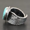Close up of the side of the "Untamable Spirit" Ring. The band is made out of a sterling silver angel wing that curves to go towards the back of the ring and meet the other side of the band. Ring is set against a dark background.