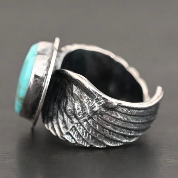 Close up of the side of the "Untamable Spirit" Ring. The band is made out of a sterling silver angel wing that curves to go towards the back of the ring and meet the other side of the band. Ring is set against a dark background.
