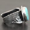 Close up of the side of the "Untamable Spirit" Ring. The band is made out of a sterling silver angel wing that curves to go towards the back of the ring and meet the other side of the band. Ring is set against a dark background.