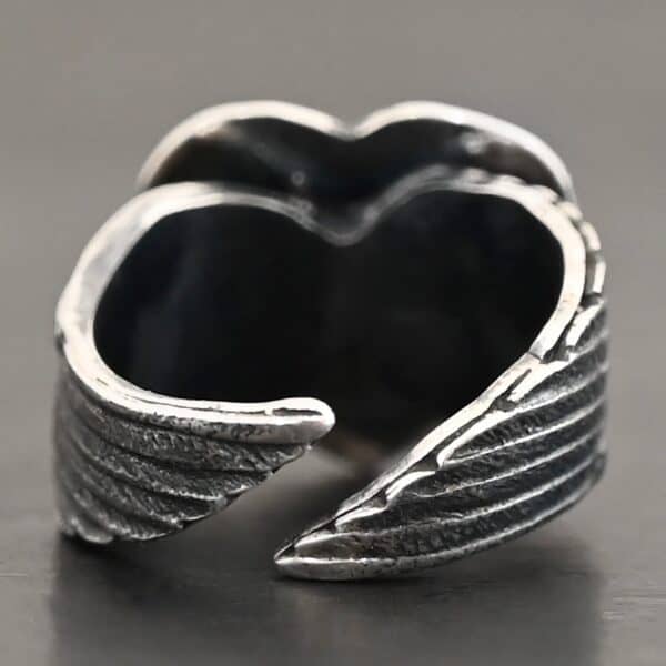 Close up of the back of the "Untamable Spirit" Ring. A curved angel wing creates each side of the band and they meet closely at the back, but do not touch. Ring is set against a dark background.
