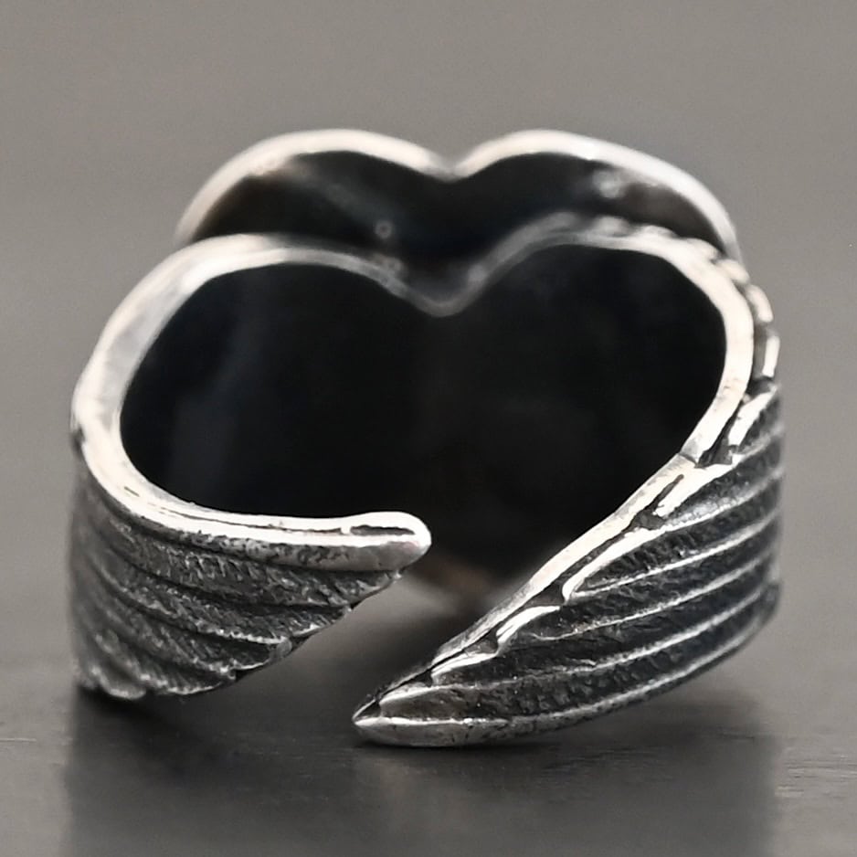 Untamable Spirit Ring Close up of the back of the "Untamable Spirit" Ring. A curved angel wing creates each side of the band and they meet closely at the back, but do not touch. Ring is set against a dark background.