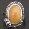 Close up of the "Marigold" Ring. Made out of sterling silver and sapphire. The sapphire is an oval shape and rosecut, and it is a dark yellow color. In the bottom left corner on the hammered sterling silver surrounding the ring are three silver balls. They are slightly curved and set next to one another so that they follow the curve of the sapphire. Ring is sitting against a dark background.