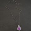 Photo of the "Ought To Do Good" Necklace. Made out of sterling silver and amethyst. The amethyst is a triangle shape but with curved points. The bottom of the amethyst has three silver dots in a straight line that go across the flat bottom. The rest of the silver setting is hammered. There is a loop on the back with three jump rings that are attached to the chain of the necklace. Necklace is laying against a dark background.